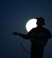 Silhouetted cowboy playing guitar in moonlight, creating a dramatic musical scene.